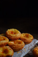 pile of egg tarts in a wire cooling rack against dark background  