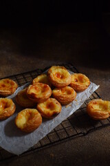 pile of egg tarts in a wire cooling rack against dark background  