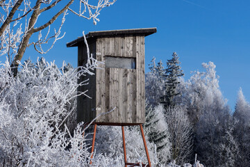 Wooden lookout tower for hunting in winter landscape with frozen trees and blue sky