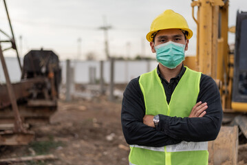 engineer man wearing face mask and working in building site. Asian worker man standing and crossed arms in construction site.