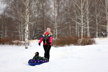Fototapeta na wymiar Woman rides a child on snow tube, family leisure in winter park