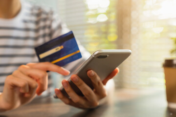 Close-up of hand holding credit card and using smartphone with online payment for shopping.