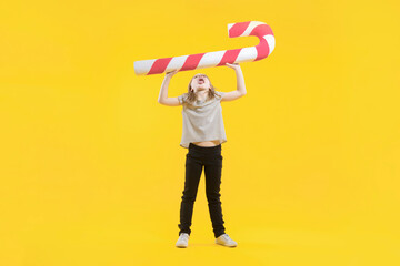 Christmas sweetness. A full-length cute teenage girl raises a huge candy above her head against a yellow background. Happy preschooler with sweets in hands. Lollipop