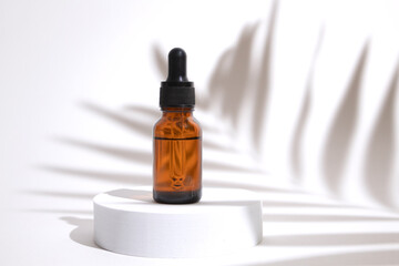 Glass dropper bottle on podium with shadow palm leaves. Cosmetic container mock-up. Creative minimalistic shot of a cosmetic product. Spa concept. Mock-up bottle for branding and label