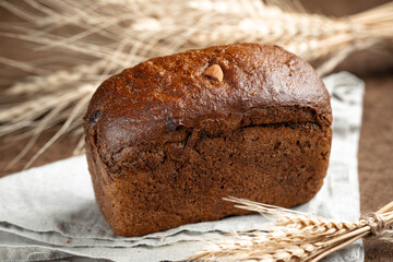 Fresh baked rye bread with dried fruits and nuts on brown background