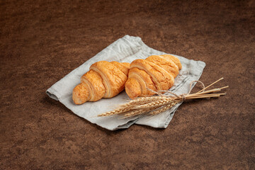 Two croissants with spikelet of wheat on brown background