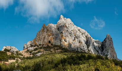 Mountain peak among green trees. Blue sky with white clouds. High quality photo