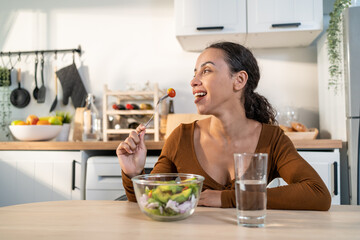 Latino attractive woman wear apron eat green salad in kitchen at home. 