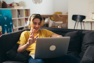 teenage boy with sitting on a sofa and using laptop computer at home for video chatting © cherryandbees