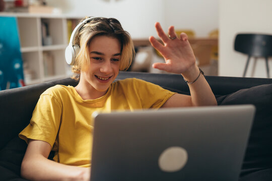 teenage boy with sitting on a sofa and using laptop computer at home for video chatting - Powered by Adobe