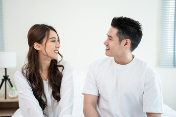 Portrait of Asian new marriage couple sit on bed and look each other.