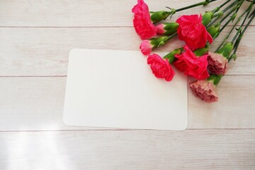 A blank greeting card with carnation flowers and on white wooden background. Mother’s Day, Father’s Day, weeding celebration background.