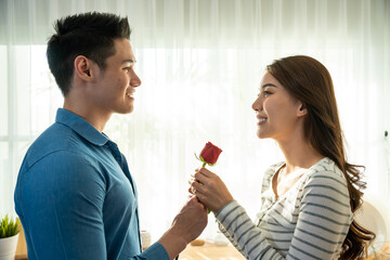 Asian young man surprise and give rose flower to beautiful girlfriend. 