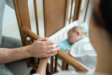 Fototapeta premium Close up of parents hand holding each other while look baby boy sleep. 