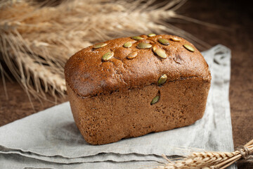 Loaf of bread with pumpkin seeds on brown background