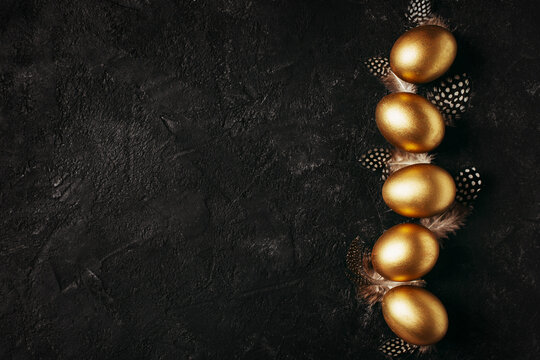Happy easter concept flat lay with gold eggs and feather on black background