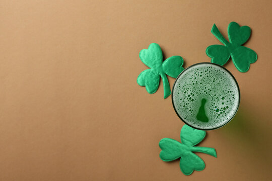 Glass of ale and clover on brown background, space for text