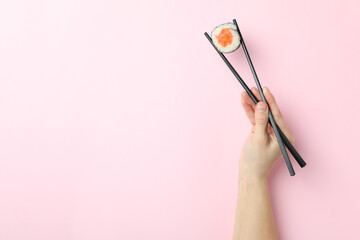 Female hand holds sushi with chopsticks on pink background