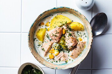 Norwegian fish soup with trout, potatoes and corn, white tile background.