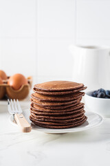 Chocolate pancakes on white plate and ingredients for cooking.
