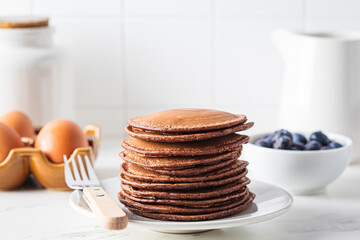Chocolate pancakes on white plate and ingredients for cooking.