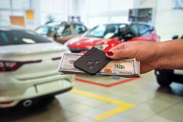 the new owner of the car holds a handful of dollars and car keys in the car showroom.
