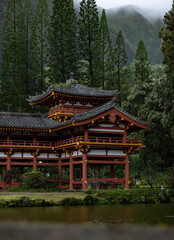 Obraz premium A part of Buddhist temple surrounded by big trees and green mountains with clouds