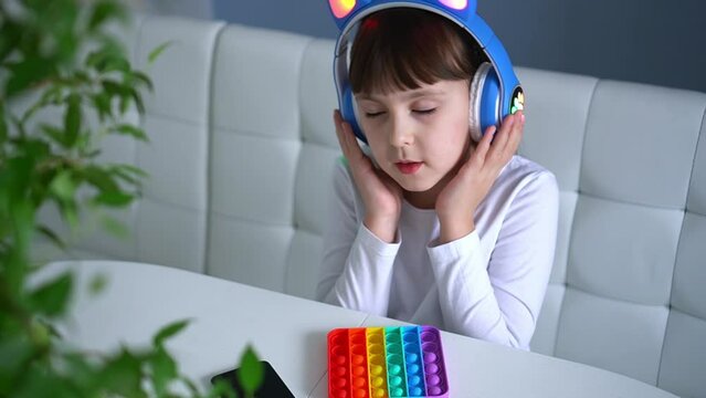 Baby girl playing with rainbow pop it fidget and listening music with headphones