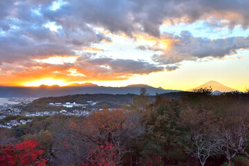 夕陽が山に沈みオレンジ色の光を富士山に照らす景色