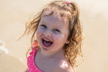 a little girl with curly blonde hair plays in the water on a sandy beach in summer. Happy child on the sandy beach. holidays and travel.