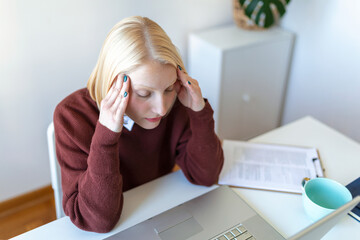Young frustrated woman working at office desk in front of laptop suffering from chronic daily...