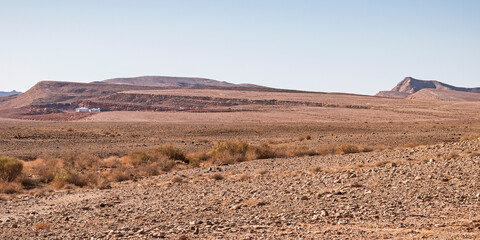 panorama of the bottom of the Maktesh Ramon crater showing one solitary campsite with sparse vegetation in the foreground and a clear blue sky in the background