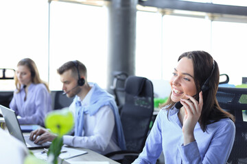 Portrait of smiling female customer service agent wearing headset with colleagues working in background at office