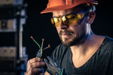 A male electrician works in a switchboard with an electrical connecting cable.