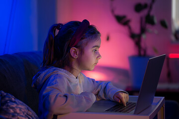 A little girl uses a laptop late at night.