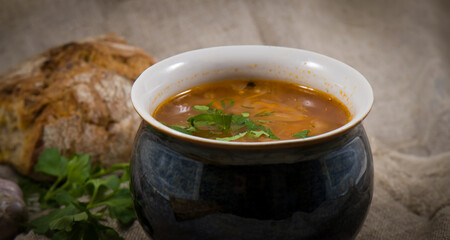 Russian traditional cuisine. A pot of sour cabbage soup, grain bread and garlic on a background of linen fabric.