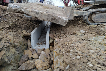 The excavator installs concrete trays for drainage of rainwater in rural areas, concrete products for drainage of water.
