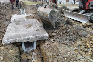 The excavator puts concrete slabs for moving through the gutter, construction work with an...