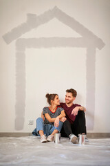 Vertical image of caucasian couple resting after wall painting of the new house