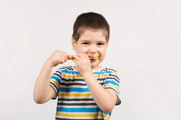 A handsome boy of 4 years old in a striped T-shirt brushes his teeth with a toothbrush on a white background and smiles, copy space for text.