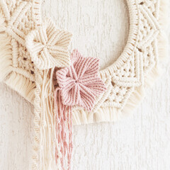 Macrame wreath with cotton flowers on a white decorative plaster wall. Natural cotton thread and rope. Eco decor for home. Creative woman hobby. Copy space