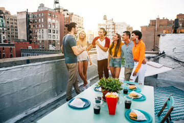 Young happy people having a barbecue dinner on a rooftop in New York.  Group of friends having party and having fun - obrazy, fototapety, plakaty