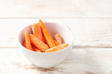 small carrot snack in a white plate on a light wooden background. healthy snack