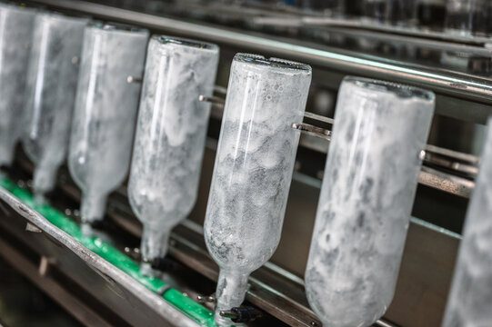 Row of empty glass bottles on automatic conveyor at plant rinsing bottles before filling