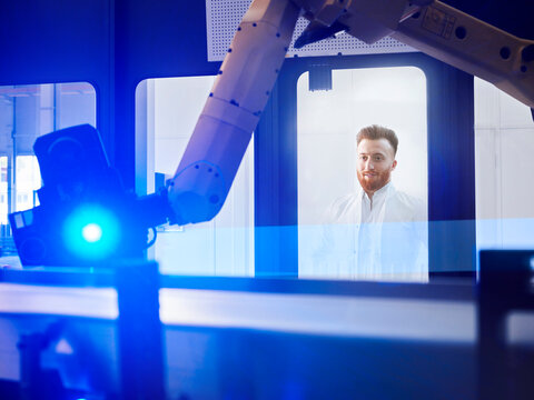 Young engineer looking at surveying robot through glass window at industry