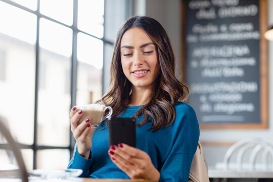 Young woman using smart phone and having cappuccino in cafe