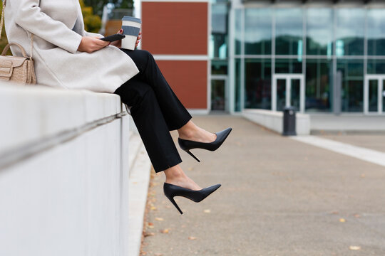 Businesswoman with smart phone sitting on wall