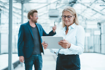 Smiling businesswoman using tablet PC with colleague in background at office