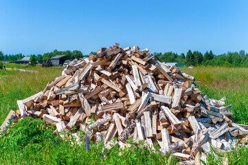 Dry firewood, chopped for winter heating of the fireplace and the house. A large pile of firewood on the meadow. Trees has been cut and split into firewood.