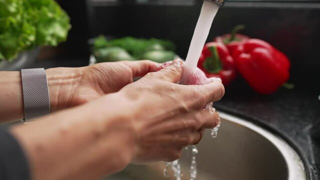 Female hands washing apple under water in sink. Washing the red apples in woman hands, slow motion.